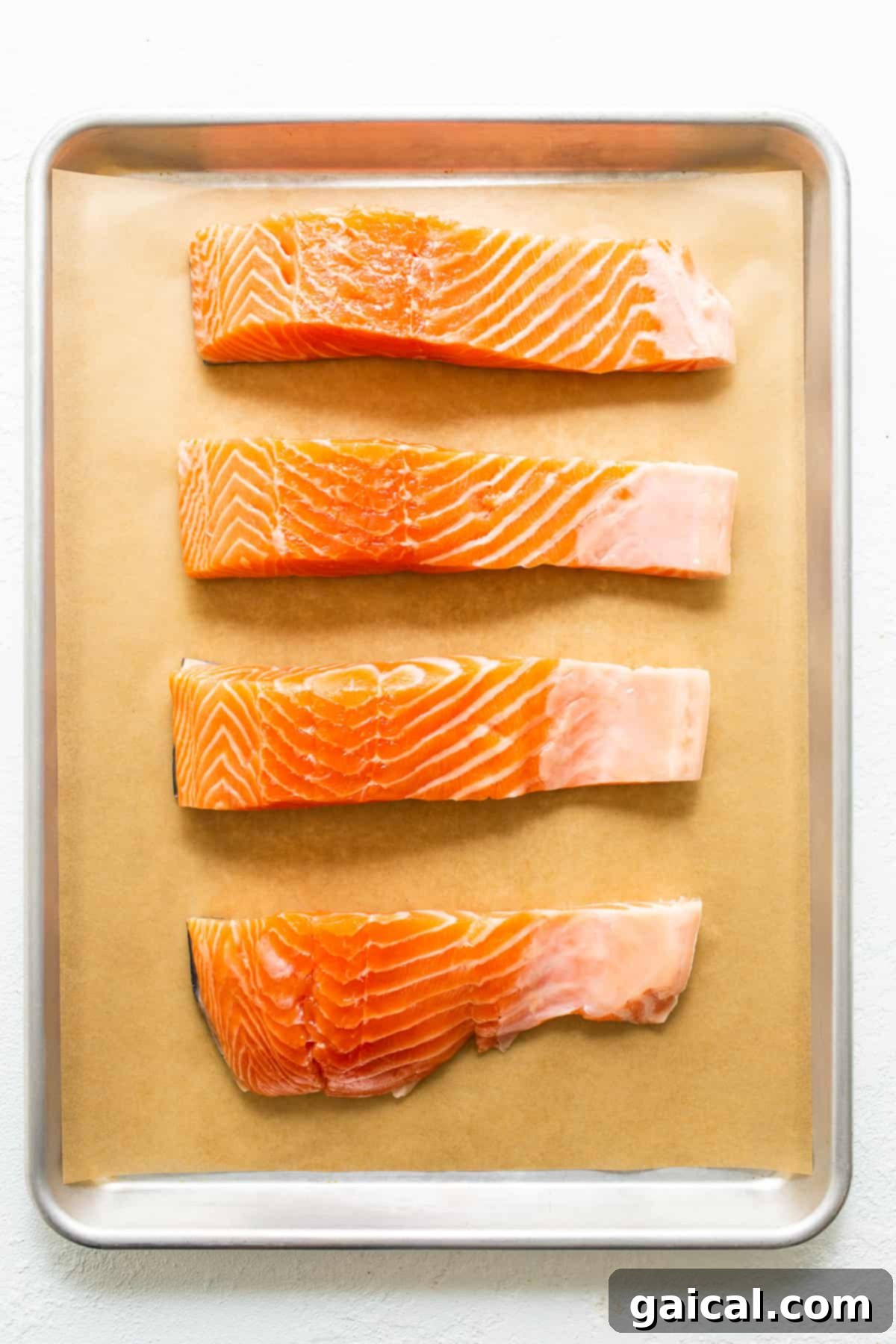 Cajun-Spiced Salmon Fillet 3 Four raw salmon fillets of similar size arranged on a parchment-lined baking sheet, ready for seasoning.