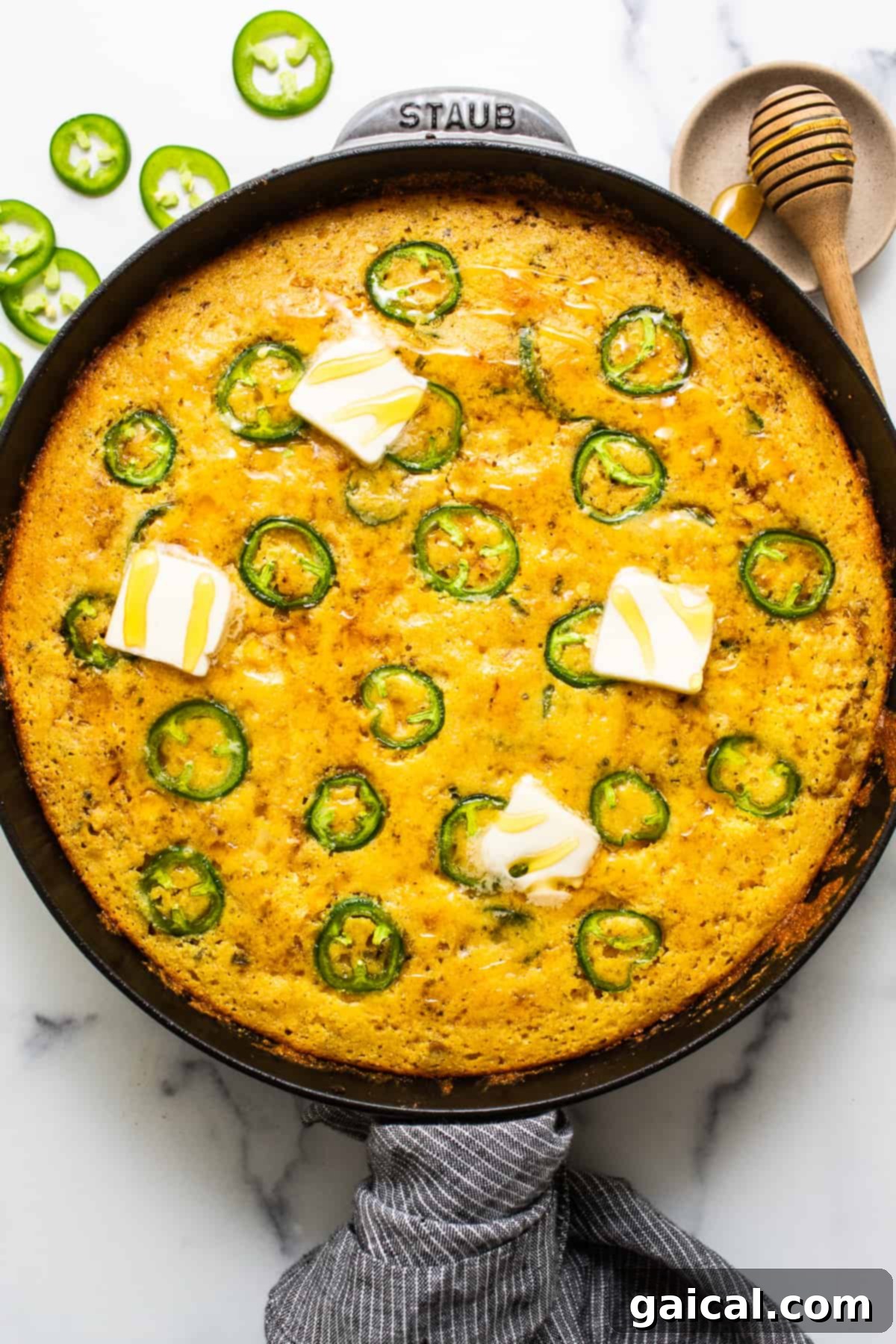This jalapeño corn pudding recipe is made completely in a cast iron skillet in under an hour. It packs the perfect combo of sweet and spicy that you'll absolutely love! Golden jalapeño corn pudding in a cast iron skillet, garnished with melting pats of butter and fresh herbs.