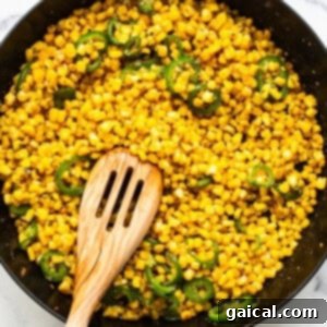 Corn and jalapenos in a skillet with a wooden spoon.