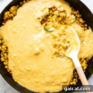 Corn on the cob in a skillet with a wooden spoon.