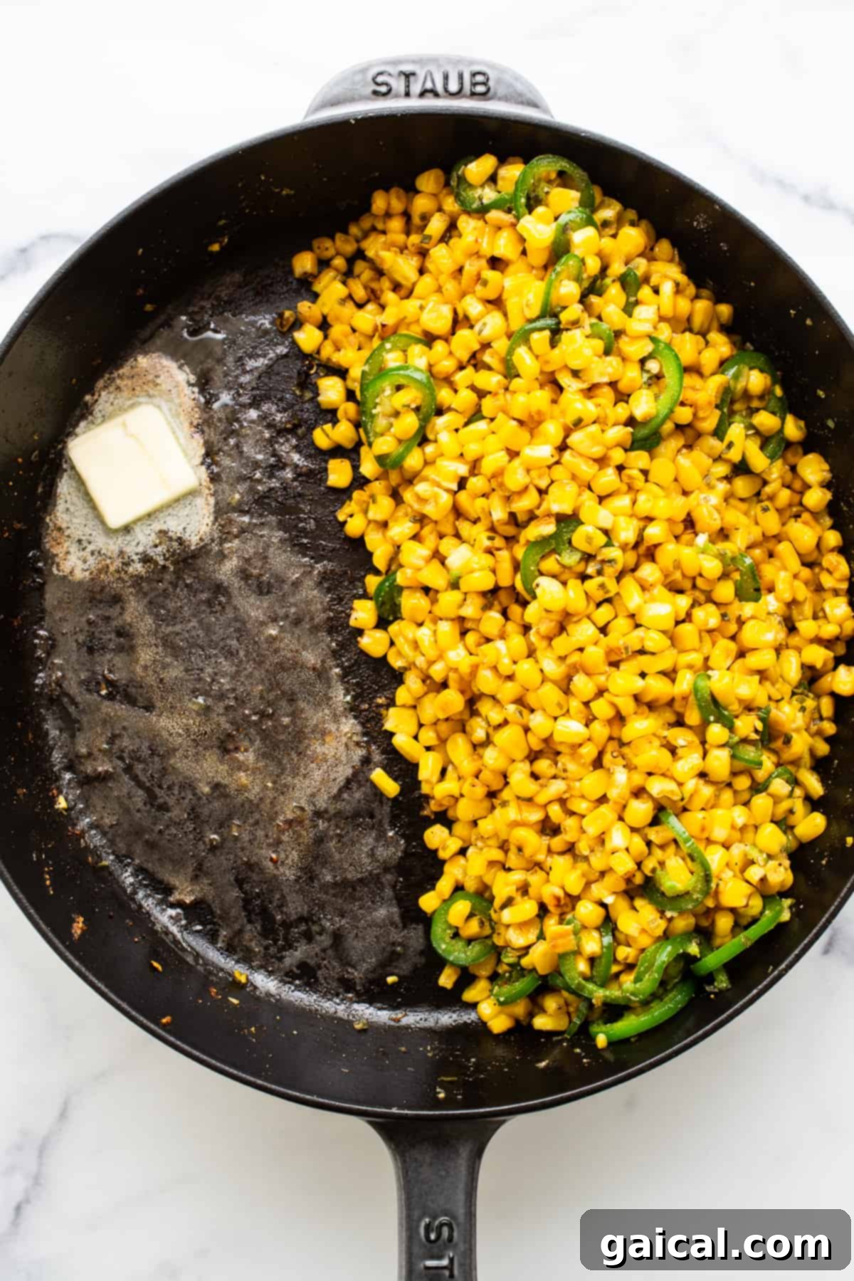 This jalapeño corn pudding recipe is made completely in a cast iron skillet in under an hour. It packs the perfect combo of sweet and spicy that you'll absolutely love! Bright yellow corn kernels and thinly sliced green jalapeños simmering in a seasoned cast iron skillet, with a pat of butter just beginning to melt.