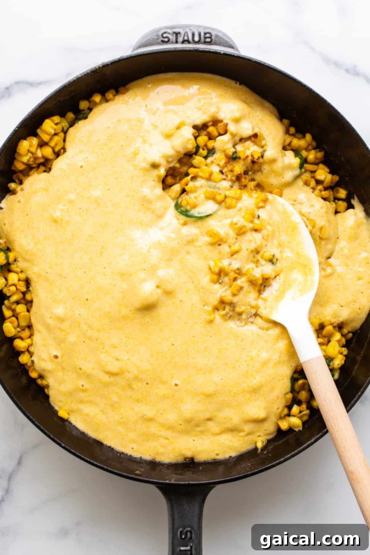This jalapeño corn pudding recipe is made completely in a cast iron skillet in under an hour. It packs the perfect combo of sweet and spicy that you'll absolutely love! The vibrant cornbread mixture, rich with corn kernels and jalapeño slices, evenly spread in a cast iron skillet and ready for baking.