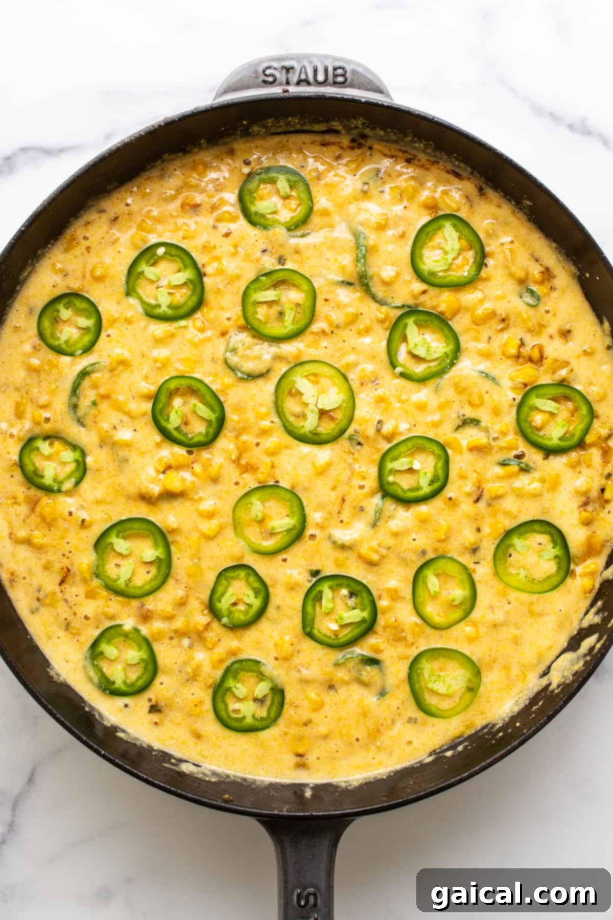 This jalapeño corn pudding recipe is made completely in a cast iron skillet in under an hour. It packs the perfect combo of sweet and spicy that you'll absolutely love! A cast iron skillet filled with uncooked jalapeño corn pudding, topped with fresh jalapeño slices, ready to be placed in the oven for baking.