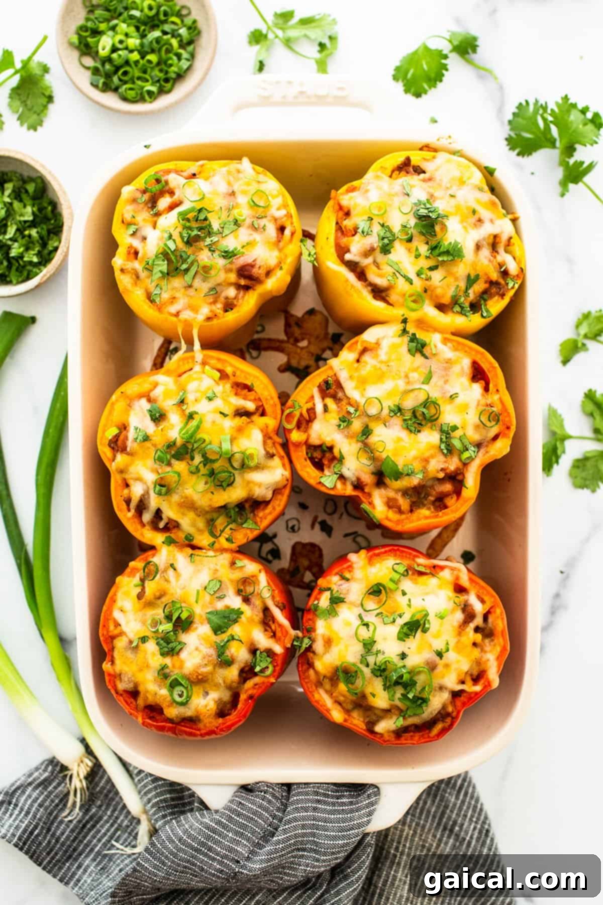 Stuffed peppers baked in a casserole dish, topped with melted cheese and fresh green onion garnish.