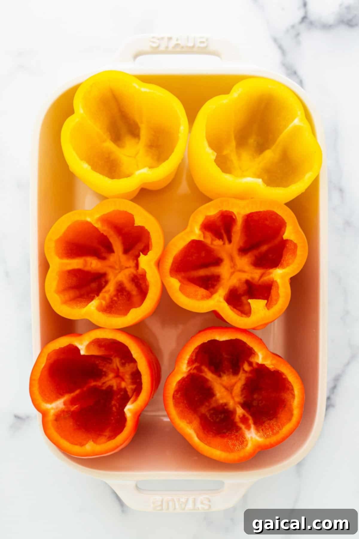 Red and yellow bell peppers, halved and hollowed, resting in a white baking dish before cooking.