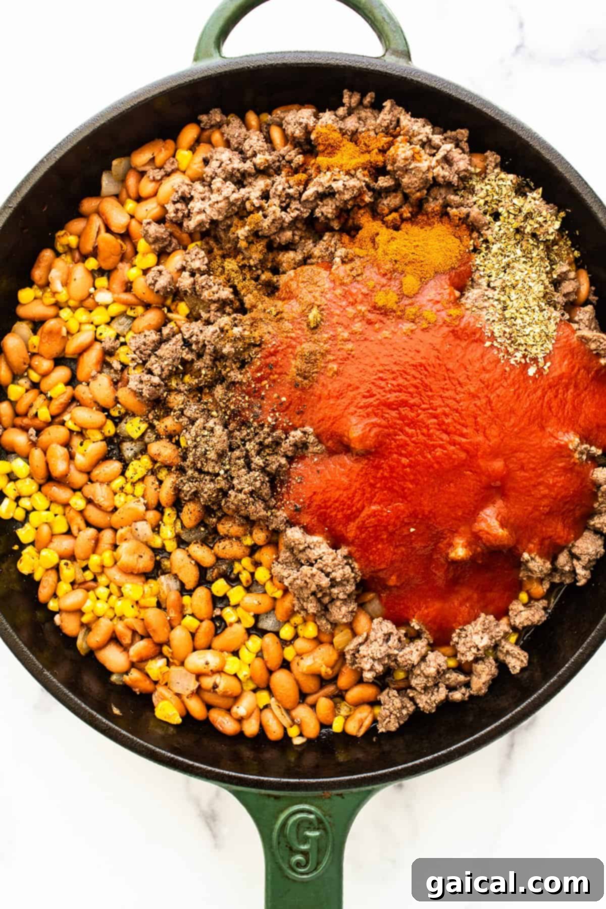 A cast iron skillet filled with a savory mixture of cooked ground beef, rice, corn, beans, and tomato sauce, ready to stuff peppers.