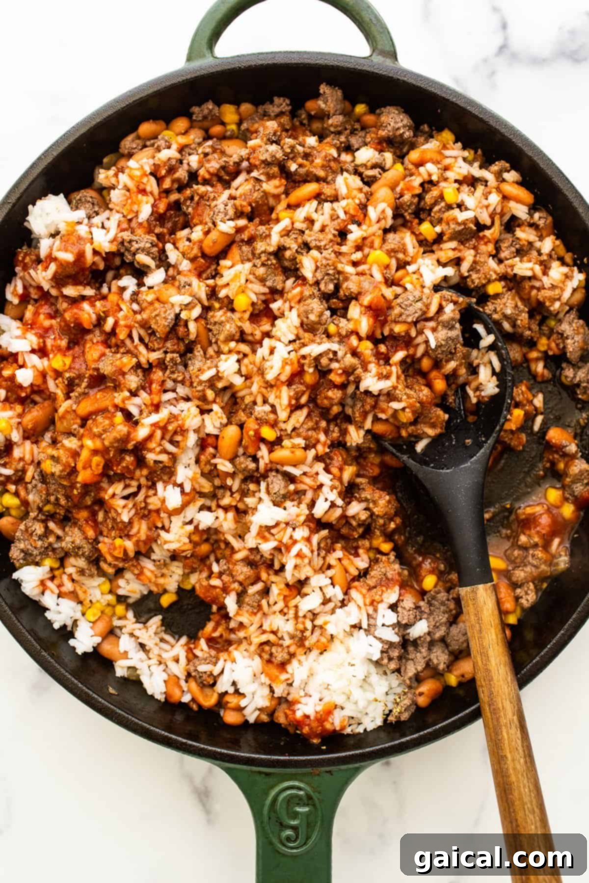 A cast iron skillet containing a vibrant mixture of ground beef, rice, beans, and tomatoes, waiting to fill the bell peppers.