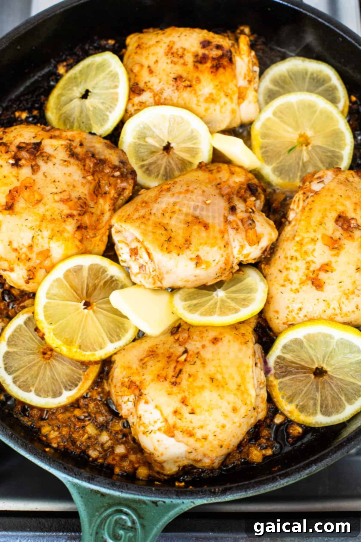 Searing Lemon Chicken Thighs Close-up of chicken thighs sizzling in a hot cast iron skillet with lemon slices and butter.