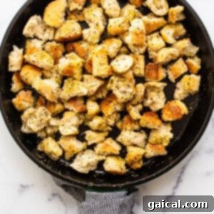 Homemade croutons being pan-fried to a golden brown in a cast iron skillet.