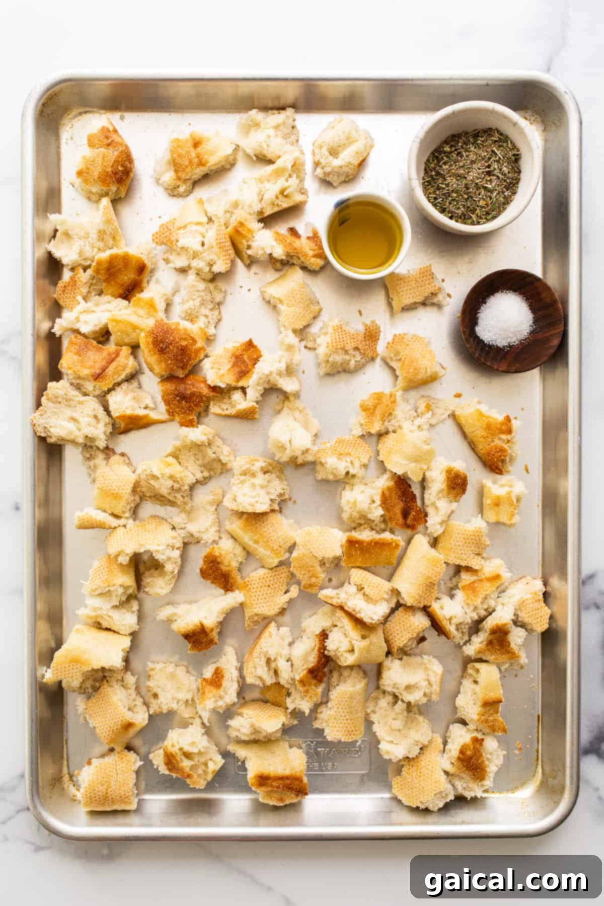 Prepped Bread and Seasoning for Croutons Rustic pieces of torn French baguette with Italian seasoning and olive oil on a baking sheet, ready for pan-frying.