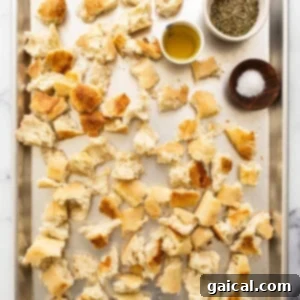 Roughly torn bread pieces on a baking sheet, ready for seasoning and frying.
