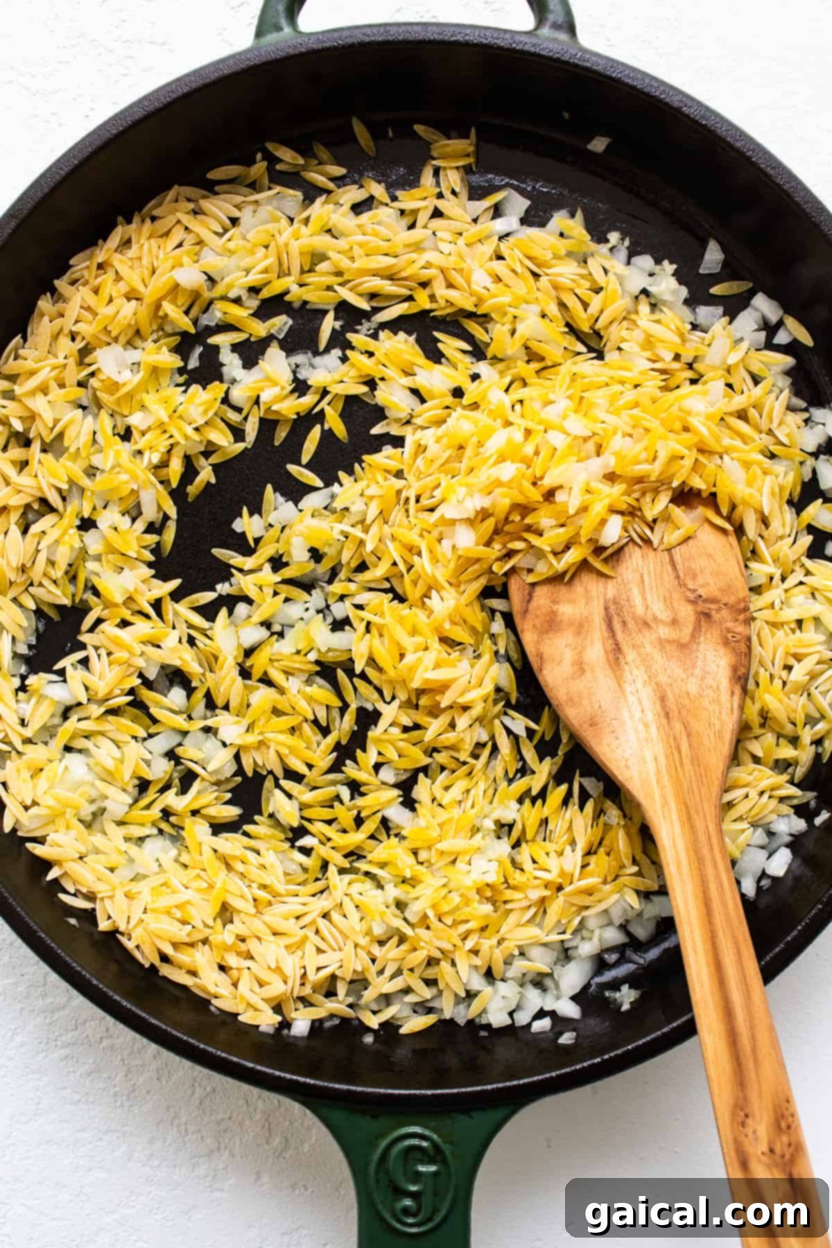 Toasting Orzo for Enhanced Flavor Golden orzo pasta being toasted in a cast iron skillet with minced onions and garlic, preparing for the casserole base.