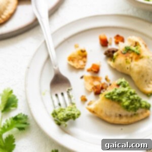 Savory Beef and Sweet Potato Empanadas 17 Cooked empanadas garnished with green sauce on a plate.