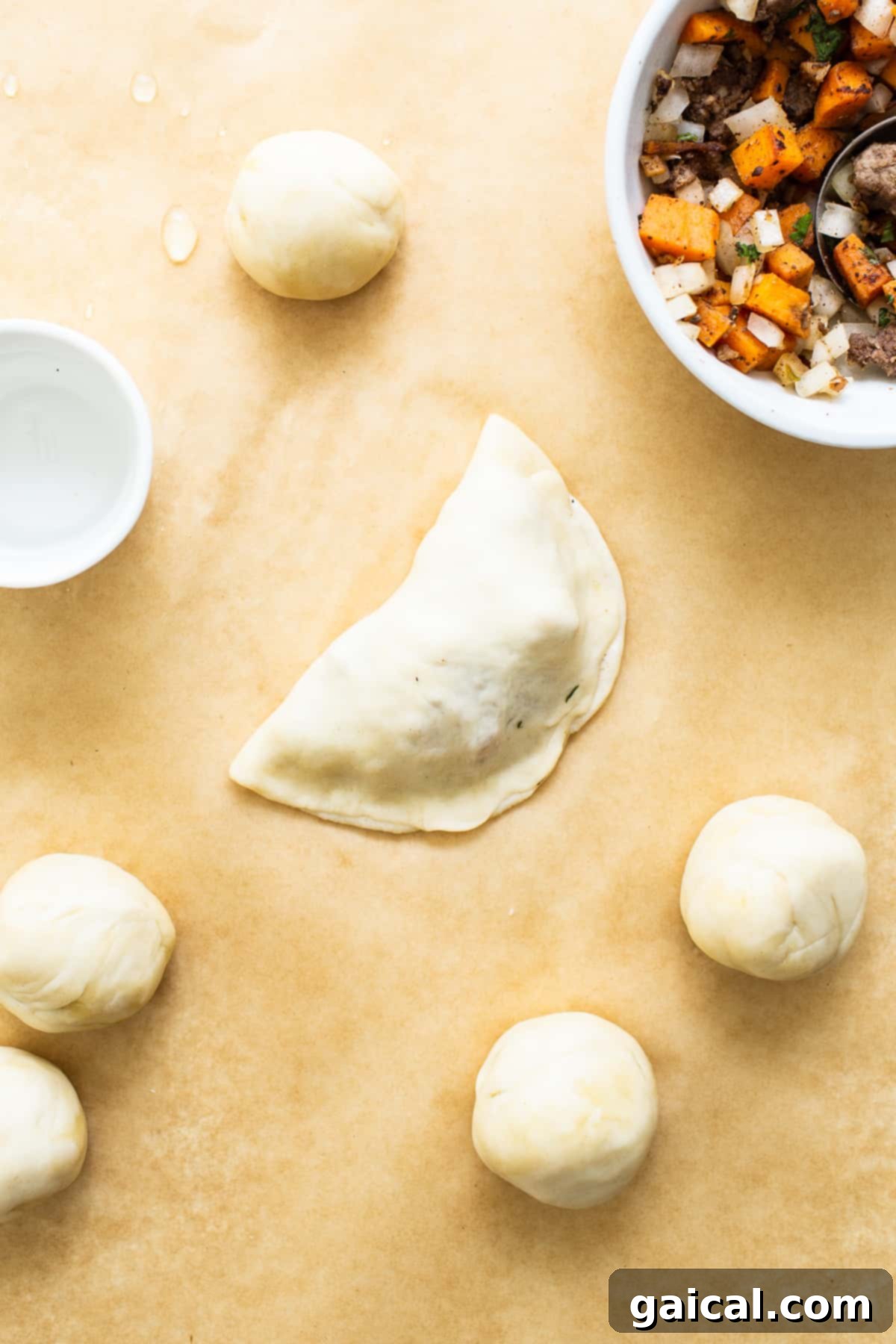 Savory Beef and Sweet Potato Empanadas 7 Assembled sweet potato ground beef empanadas laid out on parchment paper, ready for baking.