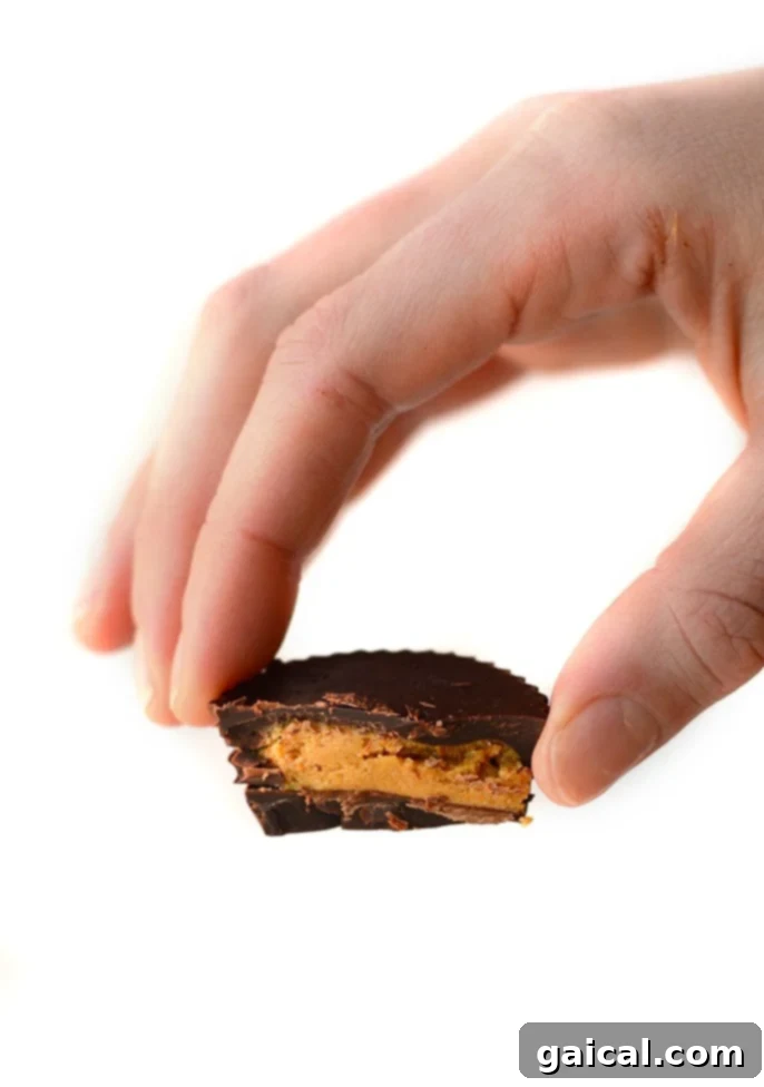 Hand holding a delicious Protein Peanut Butter Cup A hand holds a freshly made protein peanut butter cup, showcasing its layers of chocolate and peanut butter.