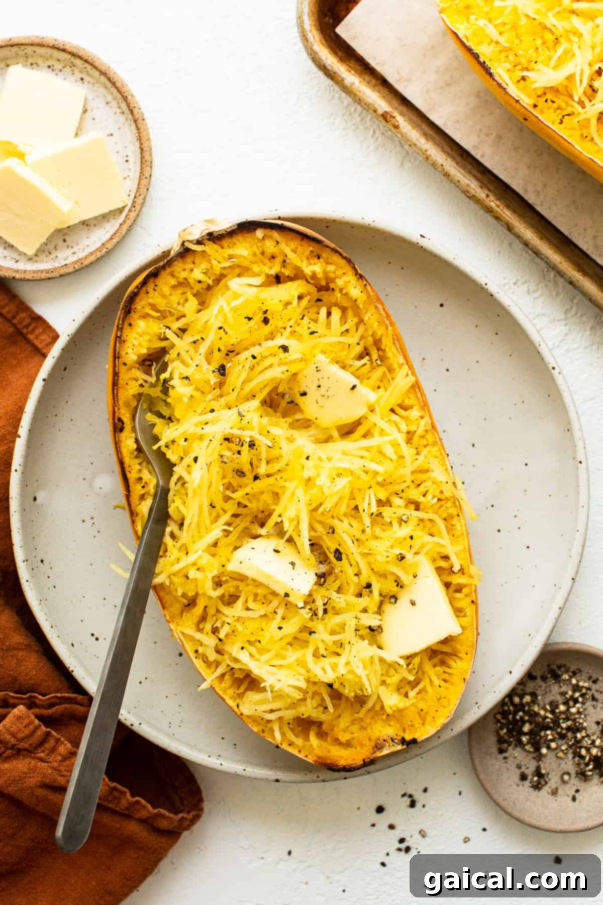 Perfectly baked spaghetti squash with a pat of butter melting on top, served on a white plate.