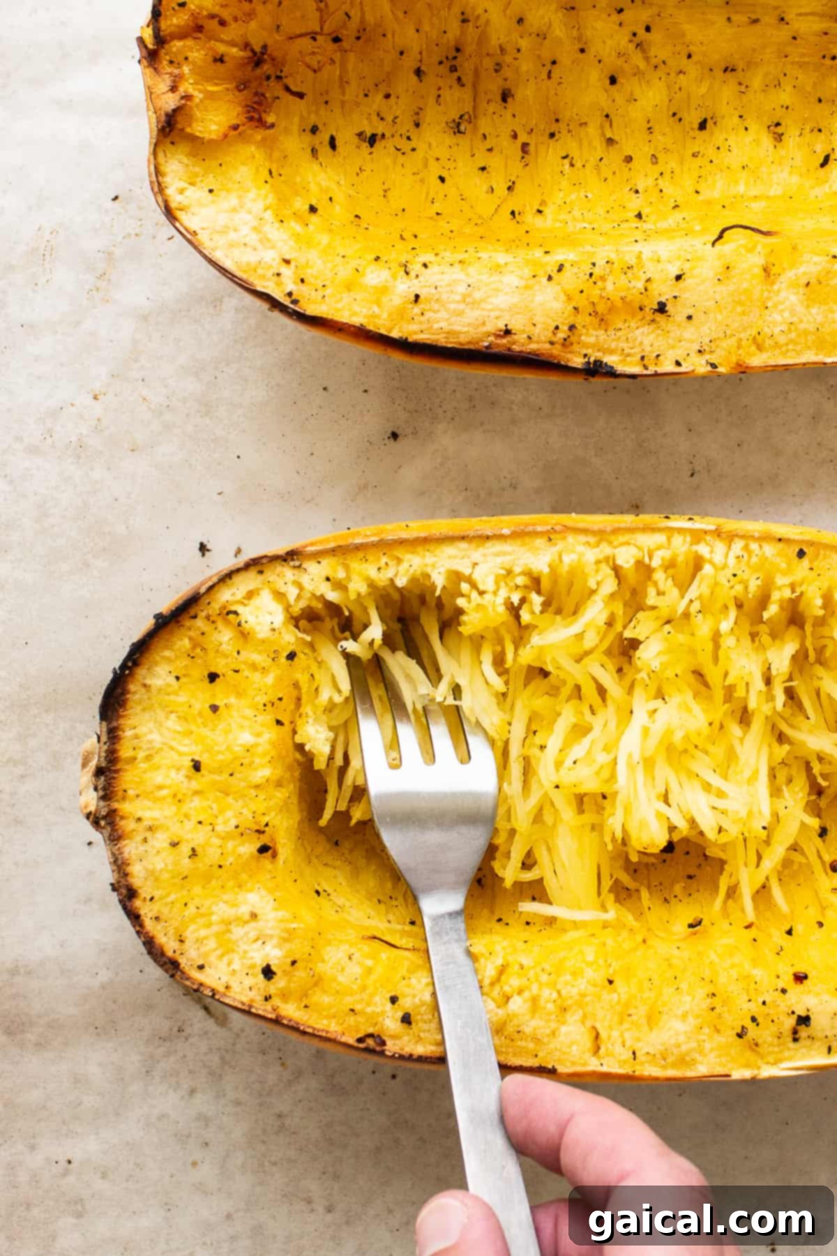 A fork scraping the tender, spaghetti-like strands from a baked spaghetti squash half on a plate.