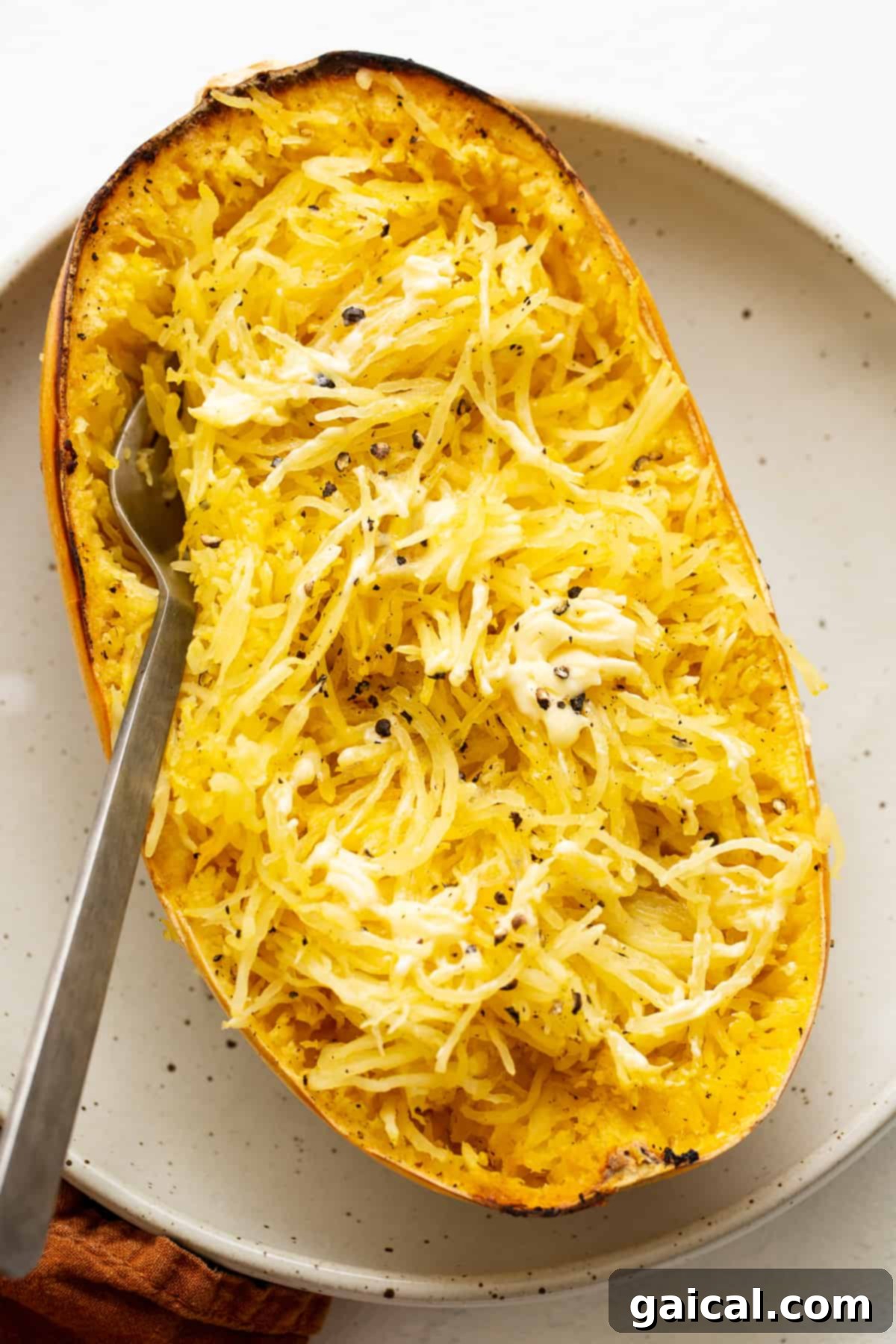 A serving of baked spaghetti squash topped with melted butter and cracked black pepper, ready to eat.