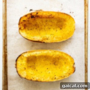 Sliced spaghetti squash halves baking on a parchment-lined sheet, cut-side up.