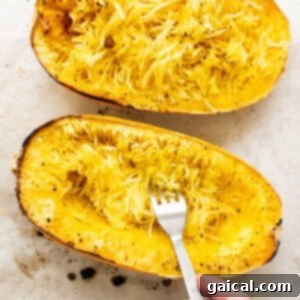 A fork scraping the cooked spaghetti squash flesh into strands.