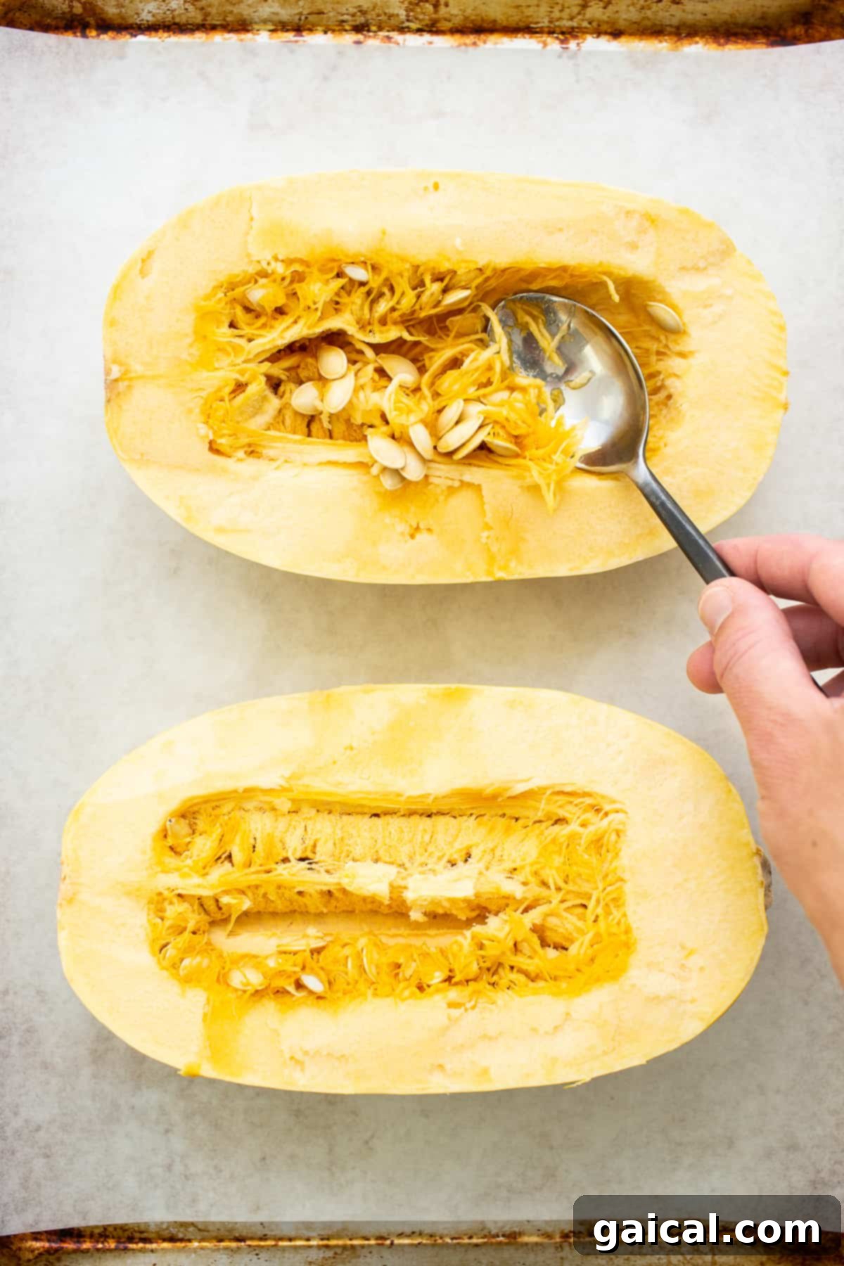 A spoon scooping out the seeds and stringy innards from a halved spaghetti squash.