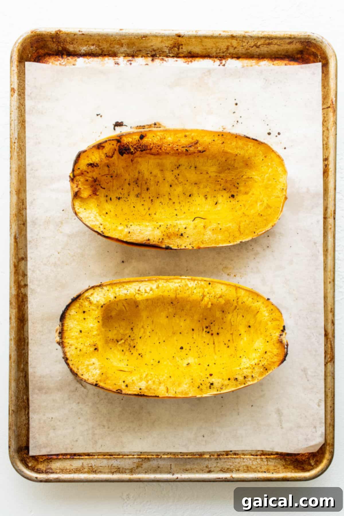 Roasted spaghetti squash halves cooling on a parchment-lined baking sheet, golden and tender.