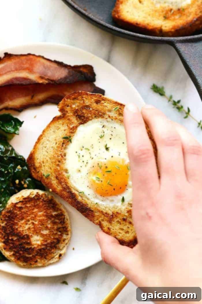 Eggs in a Basket (AKA Egg in a Hole) is such a fun twist on breakfast. Crack your egg right into a piece of toast for an open-face breakfast sandwich! Hand holding a slice of toast with an egg cooked in the center, showing a perfectly set egg yolk