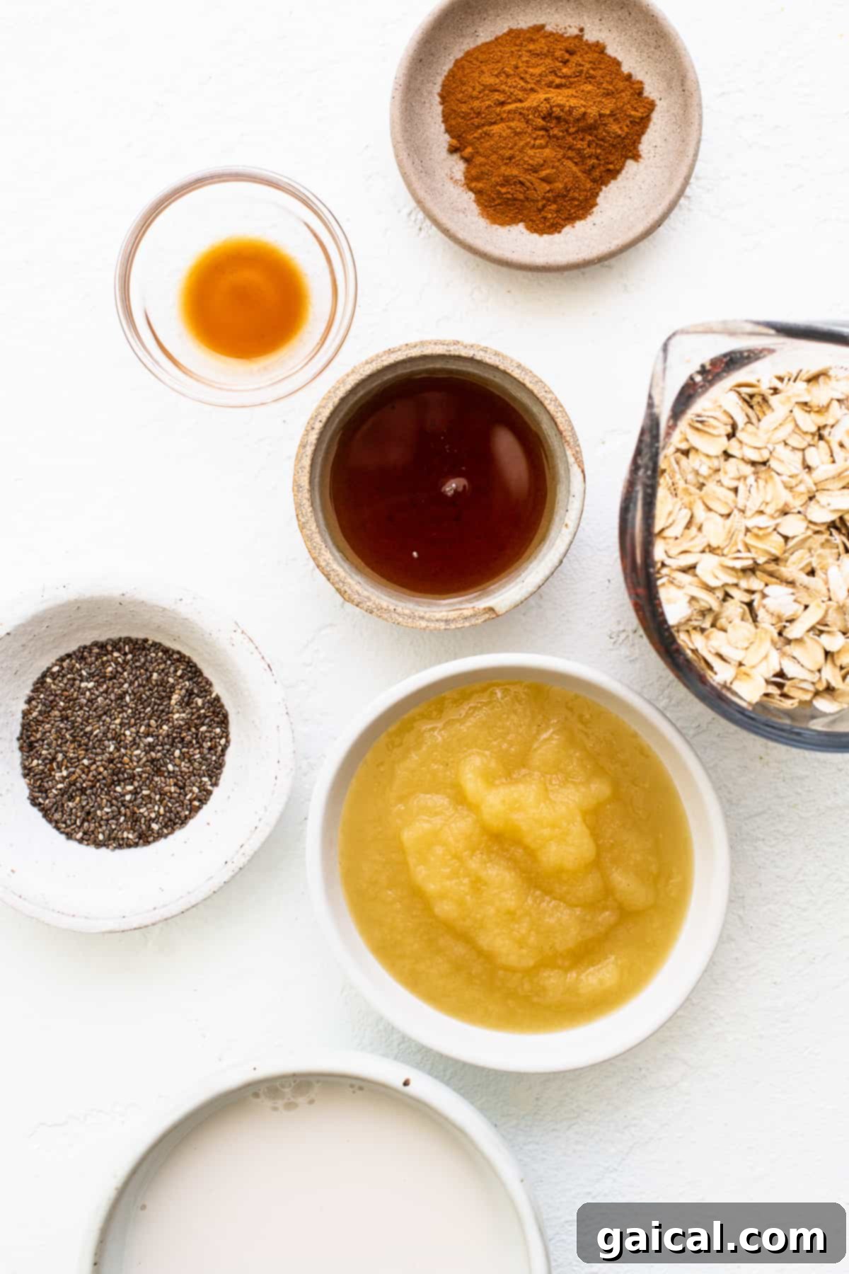A collection of ingredients for apple cinnamon oatmeal laid out in individual bowls, including oats, milk, apples, and spices.
