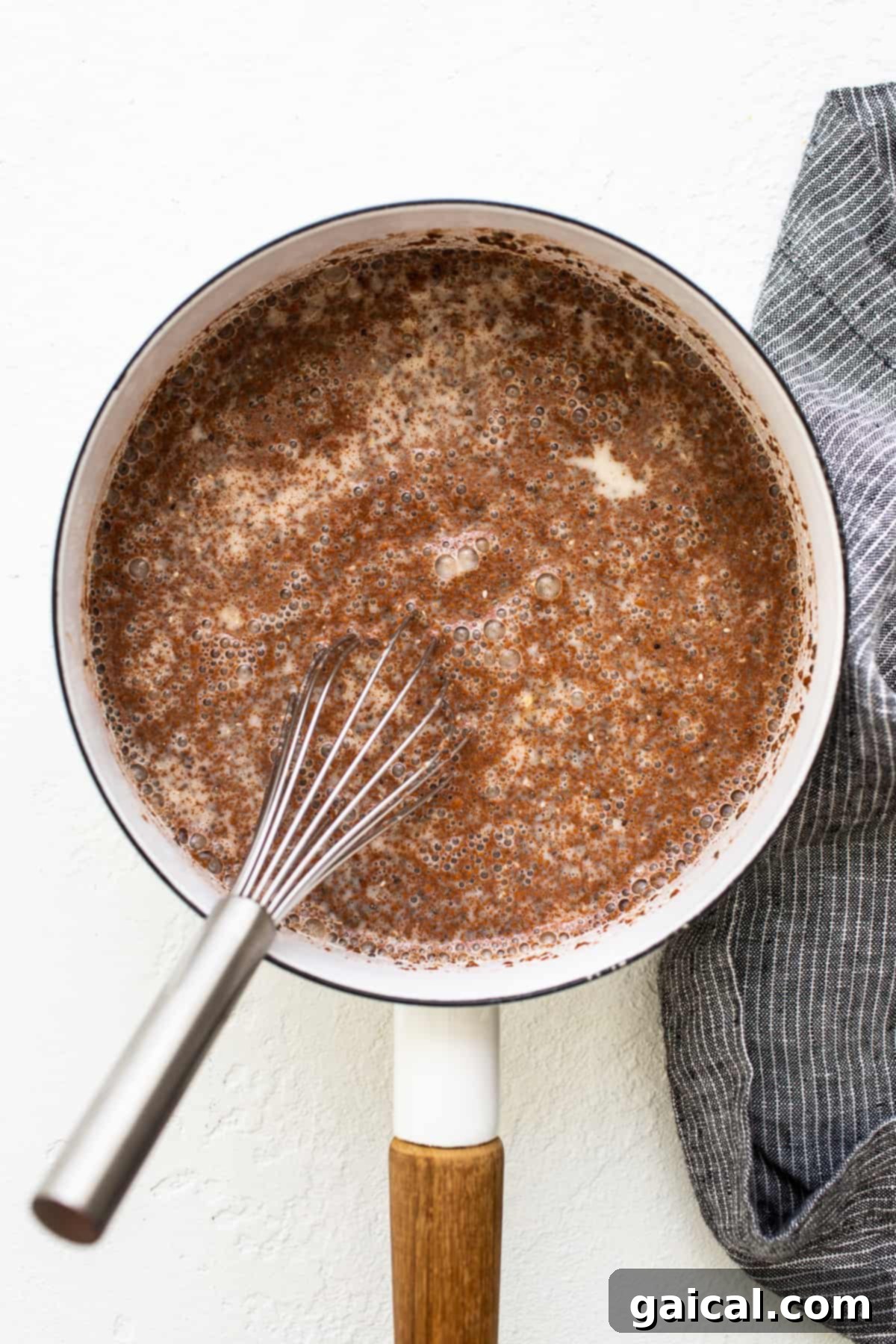 Apple cinnamon oatmeal bubbling gently in a saucepan on the stovetop, indicating it's nearly ready.