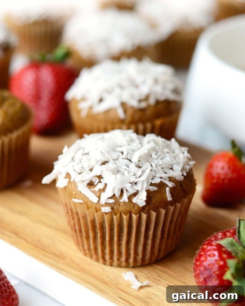 Close-up of freshly baked Strawberry Banana Blender Muffins with coconut flakes on a wooden board.