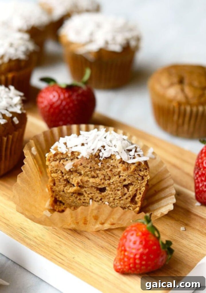 A close-up shot of two Coconut Blender Muffins with Strawberries on a rustic wooden cutting board.