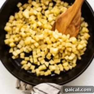 Cubed apples in a skillet with a wooden spoon.