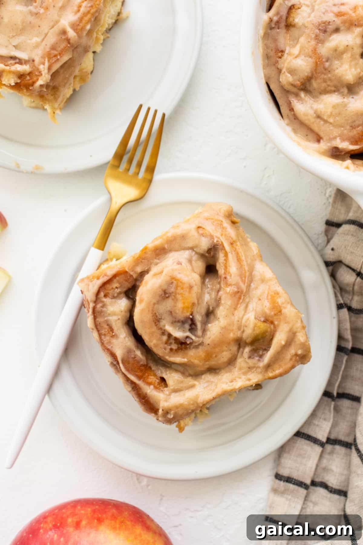 One apple cinnamon roll on a plate with a fork, showing the gooey center.