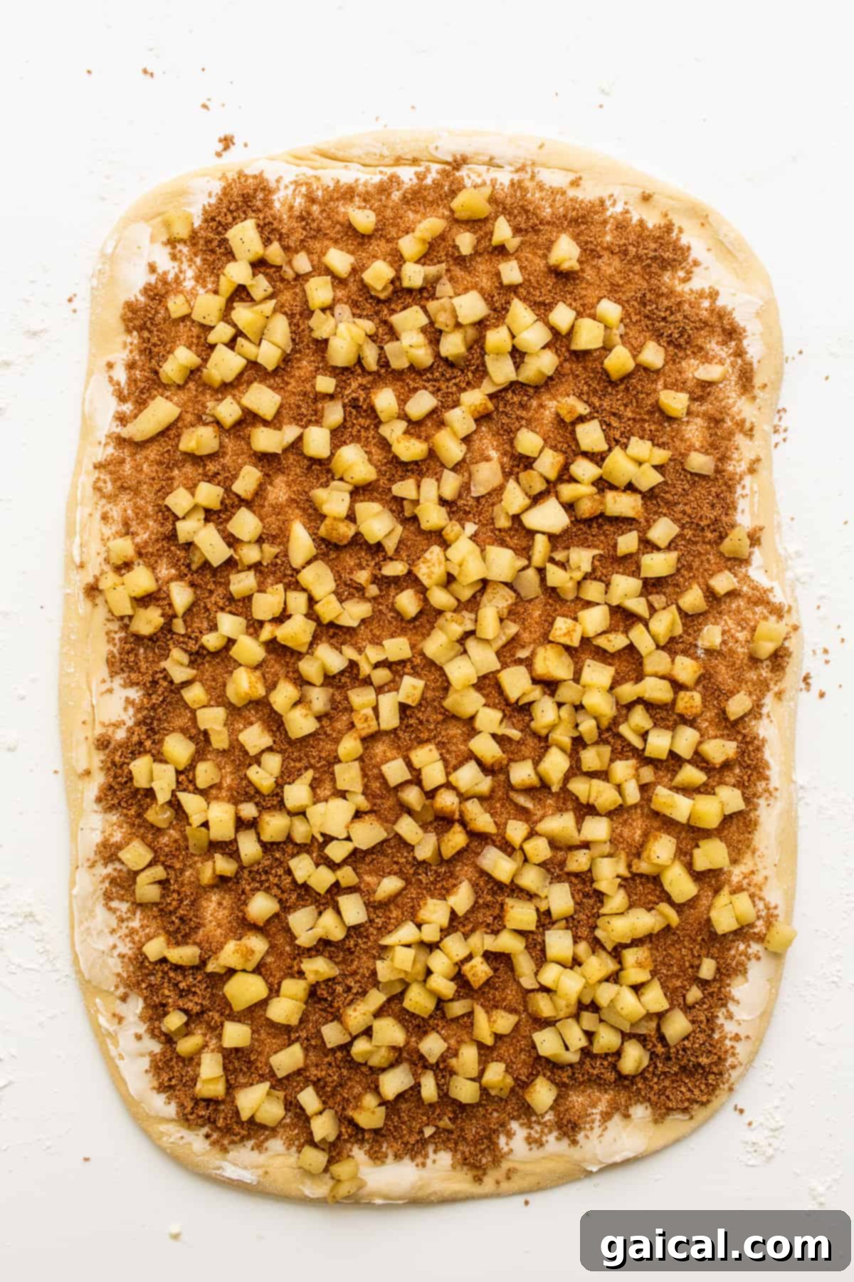 Filling for apple cinnamon rolls sprinkled generously on the rolled out dough, ready for rolling.