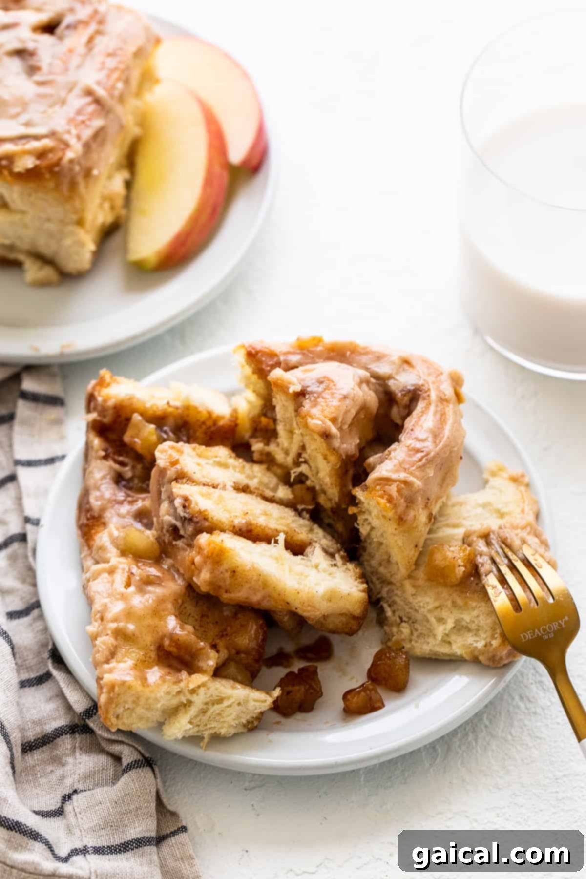 A single, perfectly frosted apple cinnamon roll on a plate with a fork, ready to be eaten.
