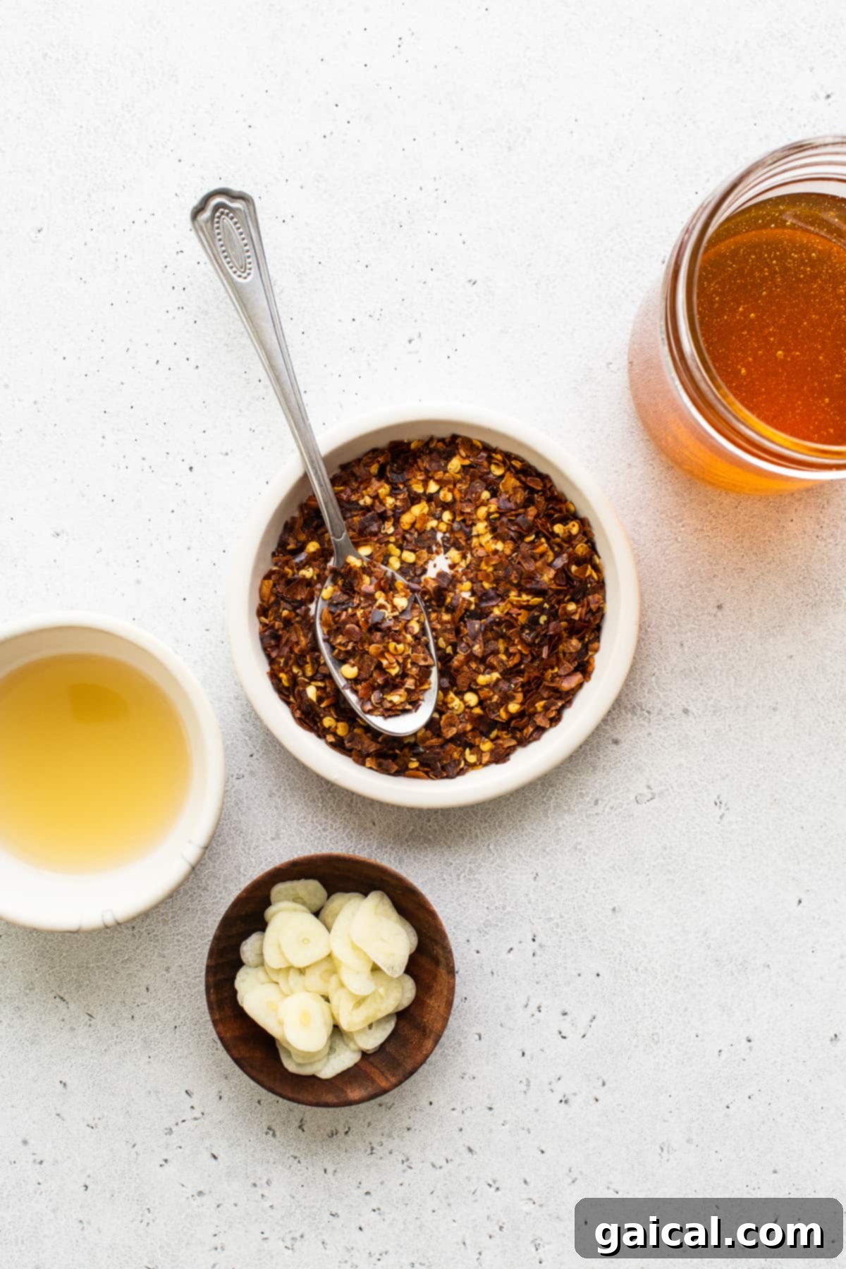 Our 4-ingredient hot honey sauce is hot, sticky and a little sweet. It's the perfect sauce to drizzle over chicken, seafood, pizza, roasted veggies and more! Bowls of honey, red pepper flakes, apple cider vinegar, and garlic cloves, ready to be combined.