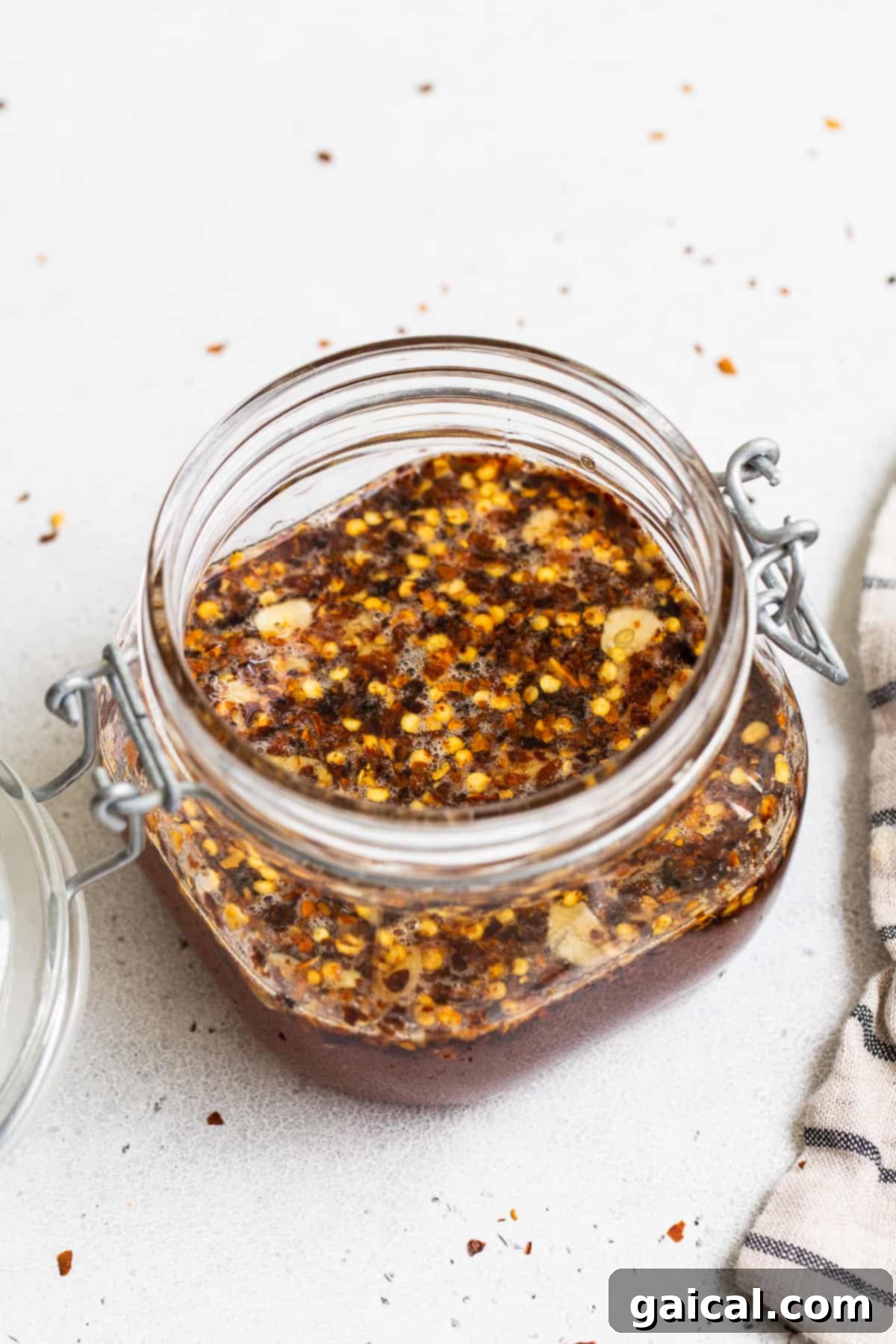 Our 4-ingredient hot honey sauce is hot, sticky and a little sweet. It's the perfect sauce to drizzle over chicken, seafood, pizza, roasted veggies and more! A mason jar of hot honey sauce with a spoon, highlighting its appealing color.