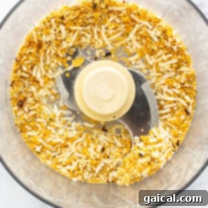 A food processor being used to make corn flake crumbs for the topping, with spices and cheese nearby.