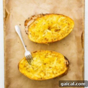 Two baked squash boats on a baking sheet with a fork, ready to be fluffed into strands.