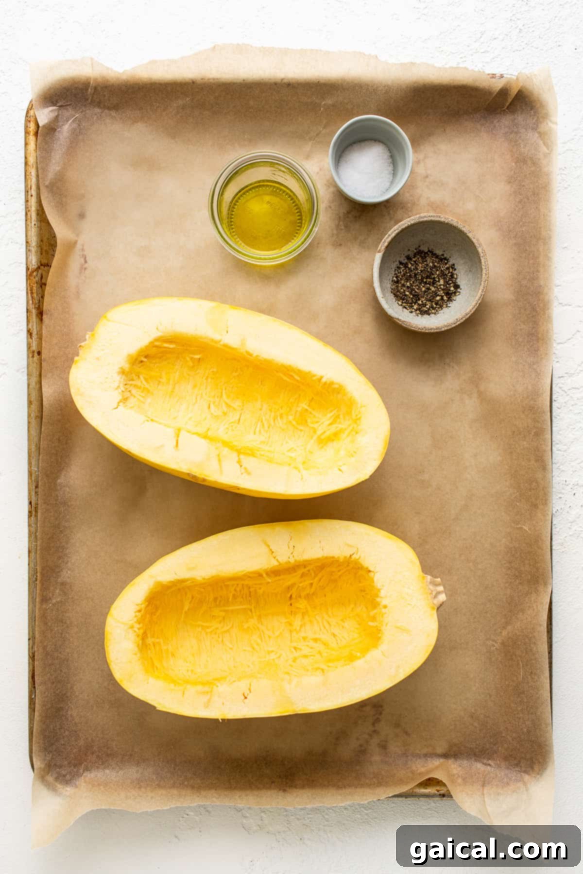 Fresh ingredients for Spaghetti Squash Mac and Cheese laid out on a baking sheet, including squash halves, cheese, and spices.