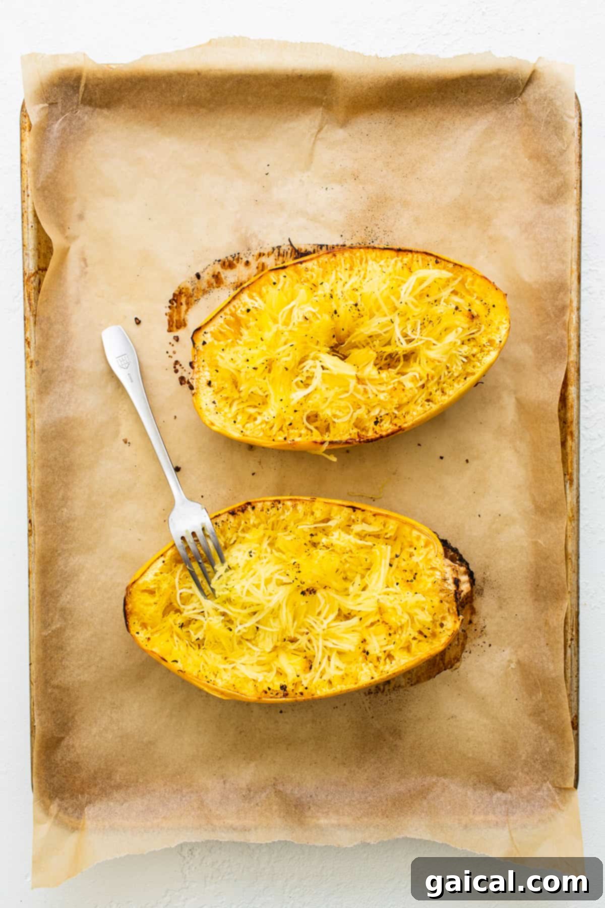 Halved spaghetti squash drizzled with olive oil and seasoning on a parchment-lined baking sheet, ready for roasting.