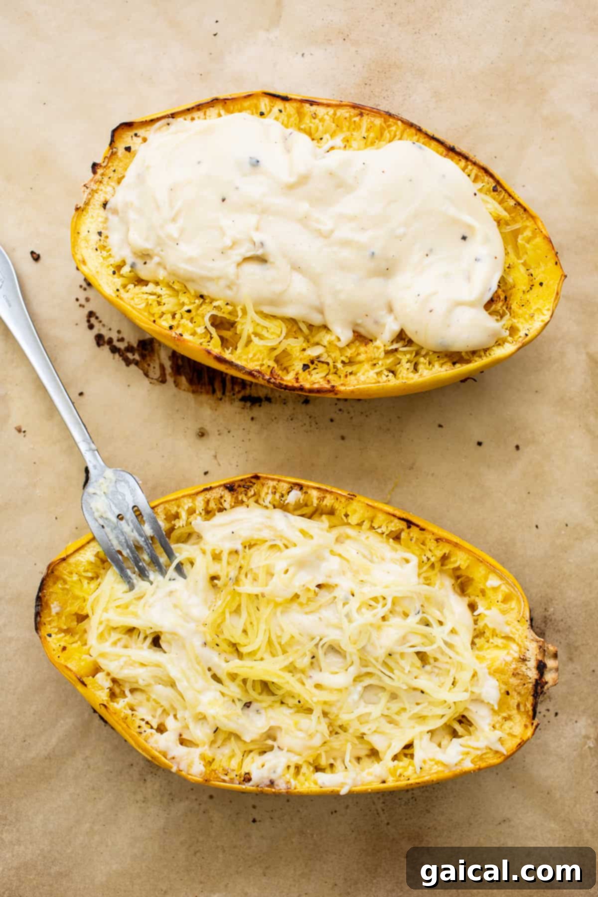 Two halves of spaghetti squash generously covered with creamy cheese sauce and ready for the breadcrumb topping, on a baking sheet.