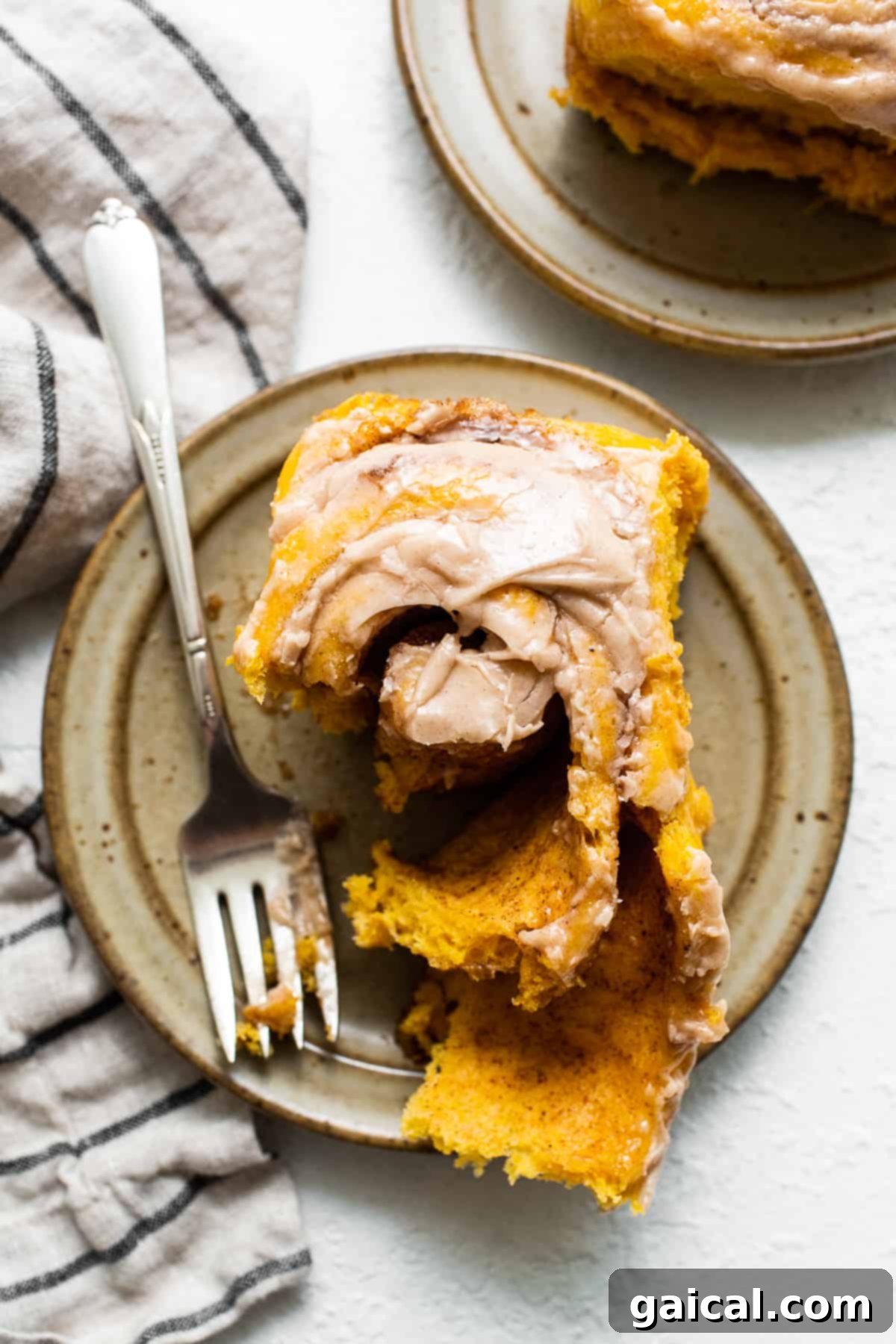 Fluffy Pumpkin Cinnamon Roll with Cinnamon Cream Cheese Frosting A single, perfectly baked pumpkin cinnamon roll on a white plate, ready to be enjoyed with a fork.