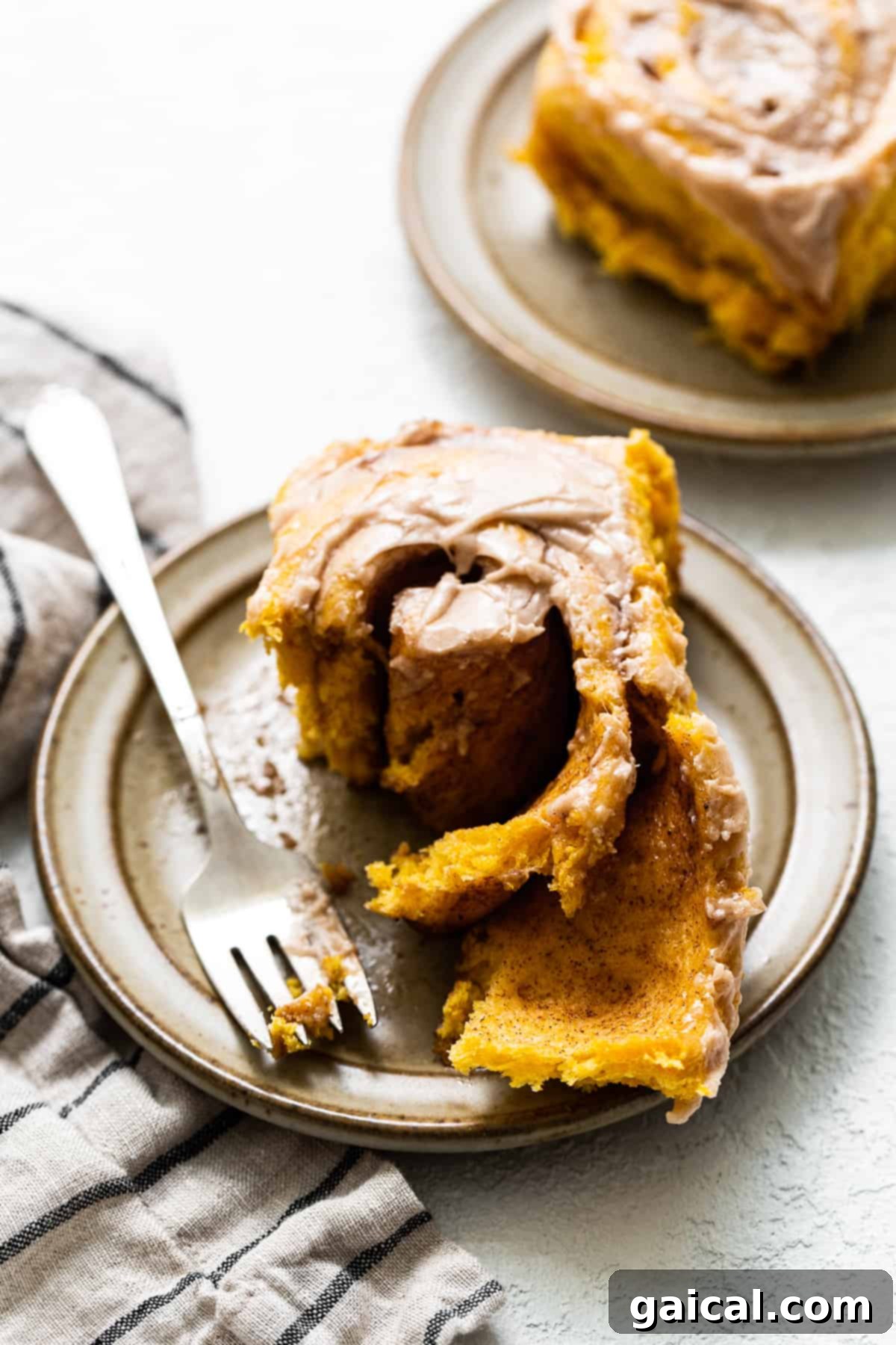 Pumpkin Cinnamon Roll on Plate A single perfectly frosted pumpkin cinnamon roll on a white plate, showcasing its golden-brown edges and soft interior.