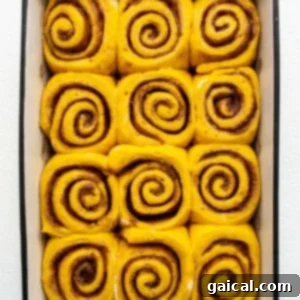 Autumn Pumpkin Swirls 10 Cinnamon rolls in a baking dish on a white surface.
