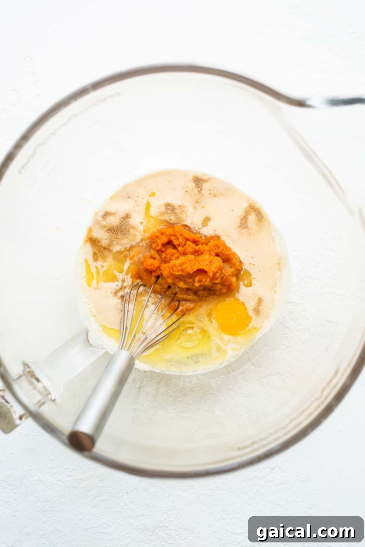 Wet Ingredients for Homemade Pumpkin Cinnamon Rolls A bowl filled with wet ingredients for pumpkin cinnamon rolls, showcasing the vibrant pumpkin puree.