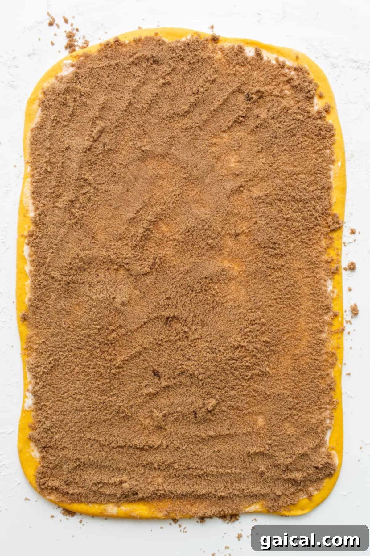 Dough with Spiced Pumpkin Filling Pumpkin cinnamon roll dough evenly spread with brown sugar and pumpkin spice filling, ready to be rolled.