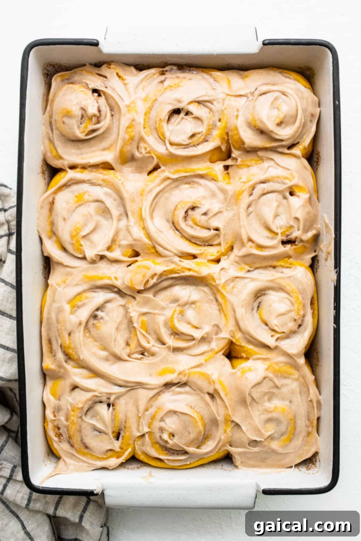 Frosted Pumpkin Cinnamon Rolls in Baking Dish A baking dish full of pumpkin cinnamon rolls generously topped with cinnamon cream cheese frosting, ready to be served.