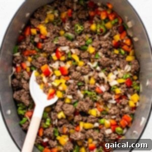 A mix of ground beef, bell peppers, and onions cooking together in a large pot.