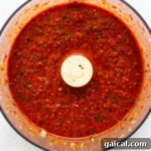 Roasted red pepper sauce being blended smooth in a food processor.